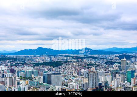 Un'ampia vista panoramica dello skyline della città di Seoul con la catena montuosa Bukhansan sullo sfondo sotto cieli nuvolosi. L'immagine acquisisce il contrasto Foto Stock