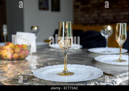 Tavolo con bicchieri d'oro, frutta e piatti bianchi. Natura morta con bicchiere di champagne dorato su piatto bianco su tavolo festivo all'interno Foto Stock