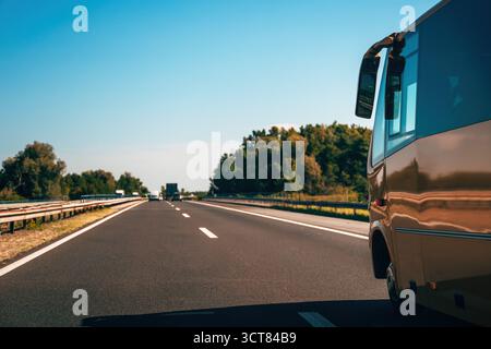 Autobus dorato sull'autostrada come se stesse correndo verso i sogni di vacanza e la fuga in vacanza. Vista laterale di un autobus che guida su strada nelle giornate di sole con traffico e. Foto Stock