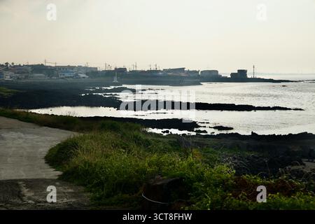 La luce della sera illumina il villaggio di Hado e un piccolo faro del porto attraverso le distese di lava marea e le acque tranquille sulla costa nord-orientale di Jeju. Foto Stock