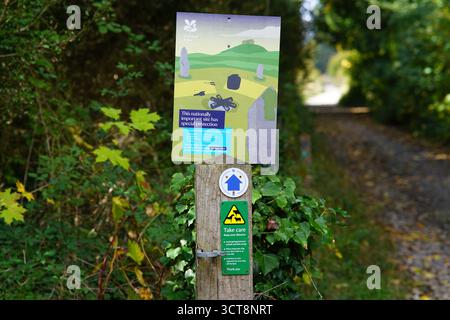 Cartello del National Trust con messaggio di conservazione lungo un sentiero rurale circondato da vegetazione e luce autunnale. Dorking, Inghilterra Foto Stock