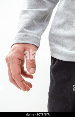Primo piano di un mans con una felpa grigia contro una parete bianca. Foto dettagliate che mostrano la consistenza del tessuto e la posa naturale, perfetta per la moda e l'adv Foto Stock