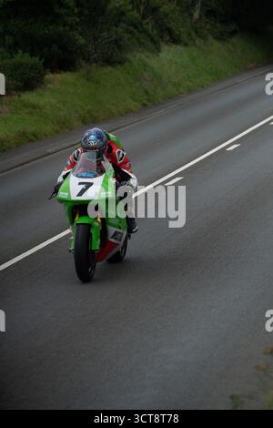 Motociclista numero 7 su una moto verde che corre in velocità lungo il circuito stradale dell'Isola di Man Foto Stock