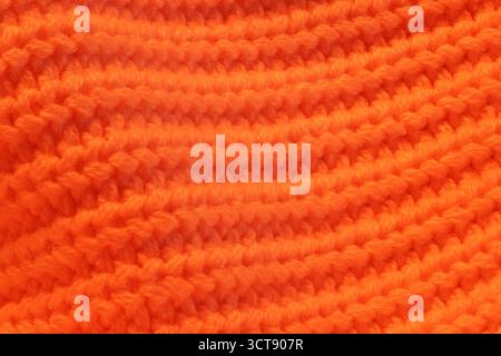 Primo piano di un maglione arancione lavorato a maglia. Il maglione è realizzato in filato e presenta un motivo a righe. Il colore arancione del maglione gli dona un caldo e un caldo effetto coccolato Foto Stock