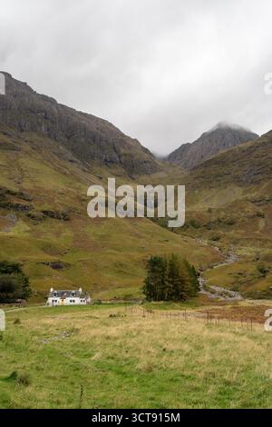 Remote Highland cottage annidato nella suggestiva valle di montagna con cascate e nuvole di acqua Foto Stock