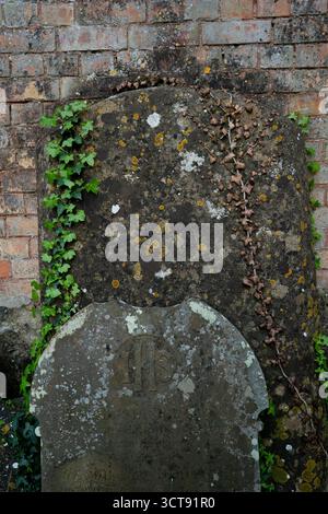 Lapide con licheni contro le vecchie mura di mattoni nel cimitero storico Foto Stock