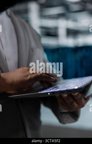 Primo piano dell'amministratore nel data center digitando sulla tastiera del notebook, scrivendo codice, perfezionando gli algoritmi. Specialista IT di server hub che utilizza script di programmazione su laptop, ottimizzando le risorse Foto Stock