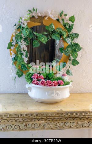 Un vaso bianco con fiori rosa siede su un tavolo accanto a uno specchio. Il vaso è pieno di rose rosa. Centro storico di Querétaro, architettura coloniale Foto Stock