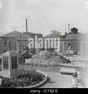 La ricostruzione di una fabbrica a Sloviansk, RSS Ucraina, durante la ripresa industriale degli anni '1950 Questa fotografia d'archivio cattura una scena di lavori di costruzione impegnativi, con nuove capriate del tetto in acciaio che vengono erette su un edificio in mattoni. In primo piano, un monumento a Vladimir Lenin si erge in una piccola piazza, un simbolo ideologico permanente che si affaccia sul caos temporaneo del cantiere. Questa giustapposizione era comune nell'era sovietica, rappresentando la ricostruzione del potere industriale della nazione sotto la bandiera del comunismo Foto Stock