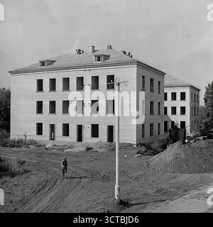 Edifici di nuova costruzione in via Chubarya (ora via Svetlodarska) nel 1950 Sloviansk, RSS Ucraina. La fotografia cattura le fasi finali della costruzione, con i lavoratori visibili sui tetti. Gli edifici in mattoni a tre piani, con i loro tetti a chiocciola e le finestre dei dormitori, sono un classico esempio di architettura della tarda epoca Stalin, costruita poco prima del passaggio alla produzione in serie di "Khrushchyovka". Il solido design neoclassico è in netto contrasto con il paesaggio fangoso e non sviluppato che lo circonda, simboleggiando un nuovo ordine che si sta creando. Foto Stock