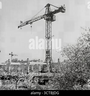 Un potente simbolo di rinnovamento e costruzione nel 1960 Sloviansk, RSS Ucraina. Questa fotografia d'archivio combina la bellezza naturale di un albero in fiore in primavera con la potenza industriale di una gru a torre in un cantiere edile. Nel quartiere di Chubarya Street (ora Svetlodarska Street), è in corso l'installazione dello scheletro di cemento di un nuovo edificio pubblico. L'immagine cattura lo spirito ottimista del boom edilizio sovietico, dove il rinnovamento della natura coincise con la creazione di una nuova e moderna città per i suoi residenti. Foto Stock