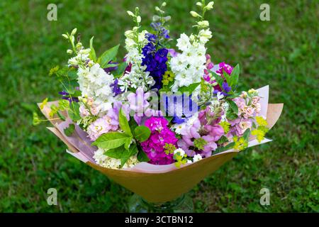 Bouquet di fiori avvolti di fiori primaverili misti. Splendidi fiori freschi rosa, bianco e blu. Bouquet di compleanno con larkspur e opaco Foto Stock