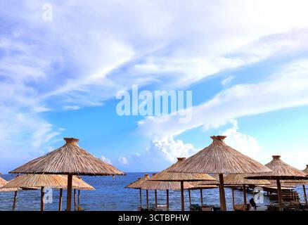 Ombrelloni da spiaggia fatti a mano da canne e mare Adriatico, Budva, Montenegro. Splendida scena con vista mare e ombrelloni realizzati con canne asciutte. Argomento o Foto Stock