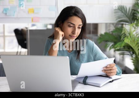 Giovane donna d'affari latina positiva che legge un documento cartaceo Foto Stock