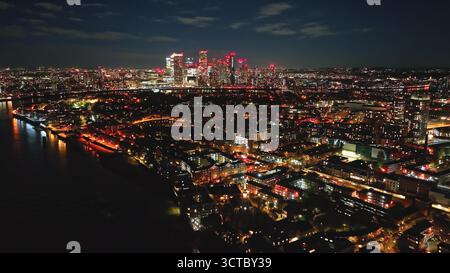 Inghilterra, Londra: Vista aerea mozzafiato di Londra di notte, con lo skyline illuminato di Canary Wharf, che crea un affascinante paesaggio urbano che si riflette sul Tamigi. Volo con drone Foto Stock