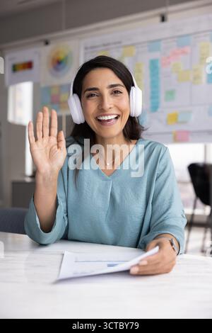 Donna professionista ispanica positiva che indossa le cuffie e saluta la mano Foto Stock