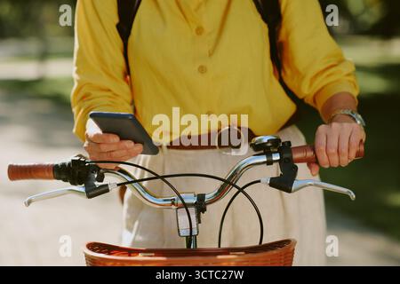 Donna caucasica di mezza età che usa lo smartphone mentre tiene la bicicletta all'aperto Foto Stock