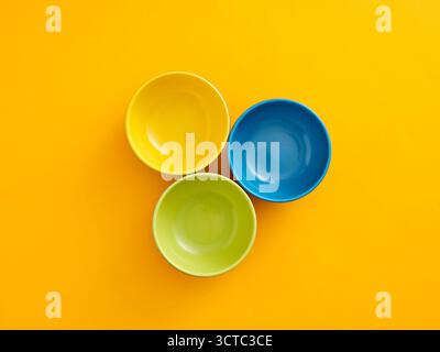 Tre ciotole in ceramica di colore giallo, blu e verde disposte su una superficie gialla brillante, creano una disposizione piatta minimalista Foto Stock