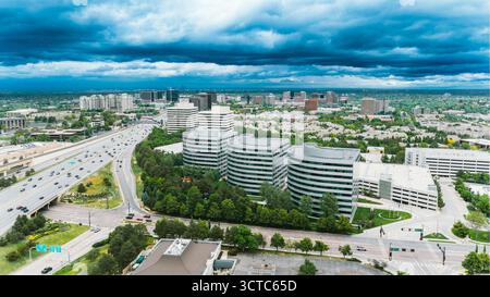 Vista aerea dell'autostrada che attraversa la città con diversi edifici di oOffice circondati da alberi sotto un cielo nuvoloso e suggestivo, Denver, Colorado, Stati Uniti. Foto Stock