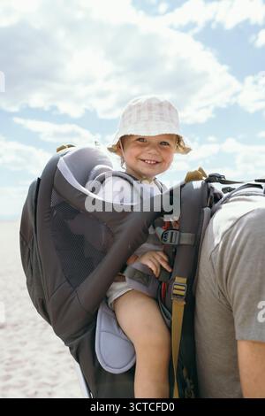 Bambino in uno zaino da trekking che si diverte all'aria aperta in vacanza Foto Stock
