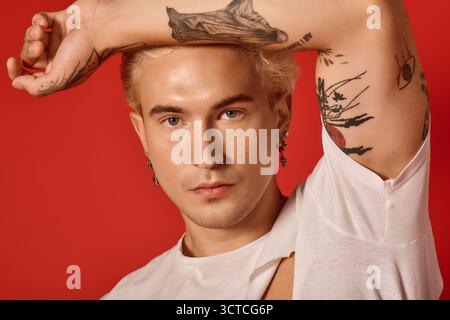 Un teenager tatuato con orecchini colpisce una posa audace, incarnando la cultura e lo stile giovanili. Foto Stock