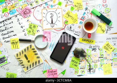 Calendario con appuntamenti e scadenze di lavoro, penne, tazze da caffè, smartphone e documenti in un luogo di lavoro disordinato. Il concetto di business batte il tempo, overwo Foto Stock