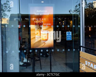 Manchester, Regno Unito - 25 settembre 2025: Poster in un negozio Starbucks in vetro che promuove sapori autunnali e bevande a base di caffè all'interno di un caffè. Foto Stock