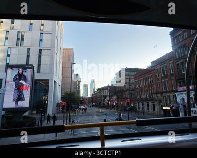 Manchester, Regno Unito - 25 settembre 2025: I pedoni passano davanti a edifici moderni e in mattoni lungo la trafficata strada di Manchester con un grande cartellone. Foto Stock