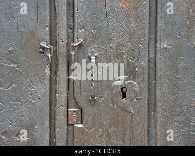 Porta in legno con serratura a cuore - primo piano di una vecchia porta in legno scuro con serratura a forma di cuore e antichi ferramenta in ferro. Foto Stock