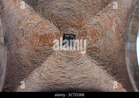 Intricata struttura in muratura sul soffitto a volta - vista ravvicinata e ad angolo basso di una vecchia volta architettonica a soffitto con un complesso edificio in mattoni vorticosi Foto Stock