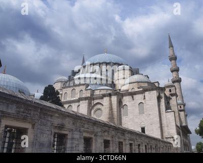 Vista sul muro di pietra della Moschea di Solimano - le maestose cupole e la torre dei minareti della Moschea di Süleymaniye sopra una storica parete di pietra, adagiata su un suggestivo clo Foto Stock