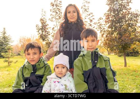 Una madre asiatica felice con i suoi tre figli, due ragazzi e una bambina, posa per un ritratto in un parco autunnale. per famiglie, genitori e stagionali Foto Stock