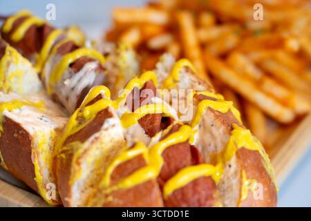 Hot dog caricati in soffici panini di pretzel con condimenti vivaci, serviti insieme a patatine fritte dorate per un pasto perfetto e appagante. Foto Stock