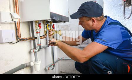 Idraulico che lavora su una caldaia, installando tubi di collegamento per un impianto di riscaldamento. Foto Stock