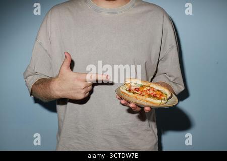 Giovane adulto che tiene il panino e punta verso il fast food Foto Stock