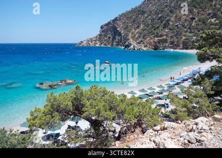 Vista della spiaggia di Apella sull'isola di Karpathos nel Mar Egeo, Grecia. Destinazione greca sul Mar Mediterraneo con gente e turisti che nuotano Foto Stock