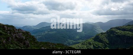 Una vista panoramica di colline verdi ondulate e montagne, alcune ricoperte di rocce, nel Gap of Dunloe nella contea di Kerry, Irlanda, sotto un cielo nuvoloso durin Foto Stock