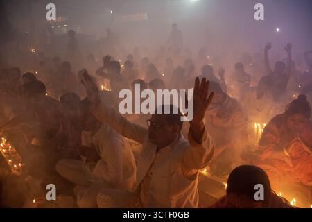 Narayanganj, Bangladesh - 09 novembre 2024: Veduta di una moltitudine di persone che alzano le mani tra la luce soffusa delle candele e il fumo etereo, creando una scena di devozione. Foto Stock