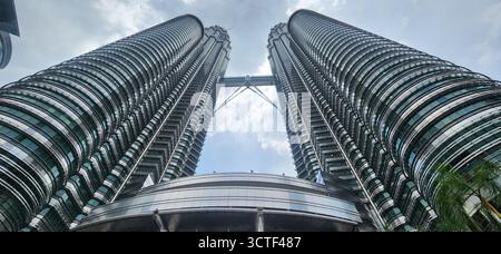 Una vista ad angolo basso dei grattacieli gemelli contro un cielo nuvoloso, che mostra l'architettura moderna. Malesia, Kuala Lumpur Foto Stock