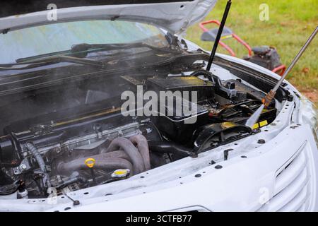 Il vapore fuoriesce dal motore dell'auto che viene pulito con un'idropulitrice in un garage all'aperto Foto Stock