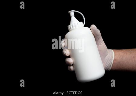 Indossare guanti in lattice con flacone a pressione in plastica bianca e tappo ugello su sfondo nero isolato. Dispenser in plastica ricaricabile per liquidi e. Foto Stock