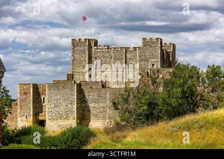 Storico castello di dover con bandiera Union Jack che sventola contro un cielo nuvoloso nel Kent, in Inghilterra Foto Stock