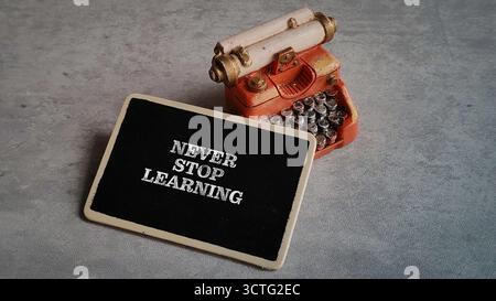 Citazione motivazionale "Never Stop Learning" sulla lavagna nera con macchina per scrivere in miniatura d'epoca Foto Stock