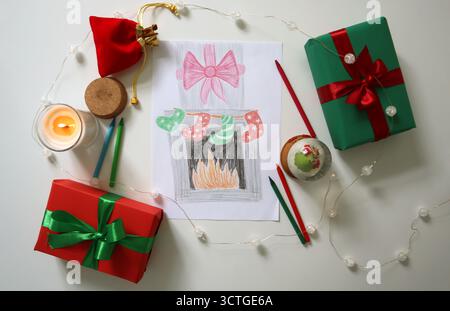 Pian camino di Natale disegnato a mano con calze, circondato da regali avvolti, candele, globo di neve, pastelli e luci da favola. Perfetto per una vacanza Foto Stock
