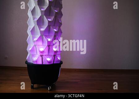 Futuristica torre idroponica verticale caratterizzata da luci blu, struttura geometrica illuminante che mette in evidenza l'innovativa tecnologia agricola interna Foto Stock