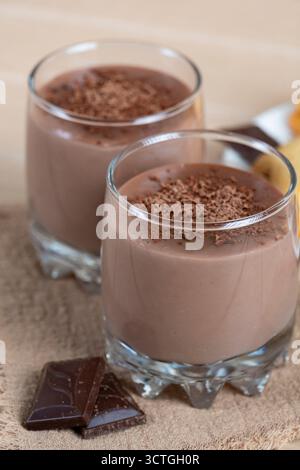 Deliziosi biscotti fatti in casa serviti con budino al cioccolato in tazze di vetro, ricoperti di cioccolato fondente grattugiato. Accogliente composizione di dessert su un tavolo di legno Foto Stock