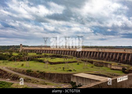 Itaipu Binacional, Brasile - 22 giugno 2025: Ampia vista dell'immensa struttura della diga di Itaipu con linee elettriche ad alta tensione che emanano dalla cresta. Foto Stock