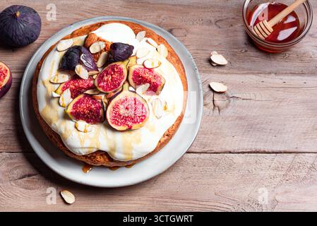 Torta di mandorle con fichi, formaggio cremoso montato e miele su sfondo di legno, vista dall'alto, spazio per copiare. Ricetta per dolci autunnali di stagione. Foto Stock