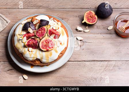 Torta di mandorle con fichi, formaggio cremoso montato e miele su sfondo di legno, spazio copia. Ricetta per dolci di stagione per le vacanze autunnali. Foto Stock