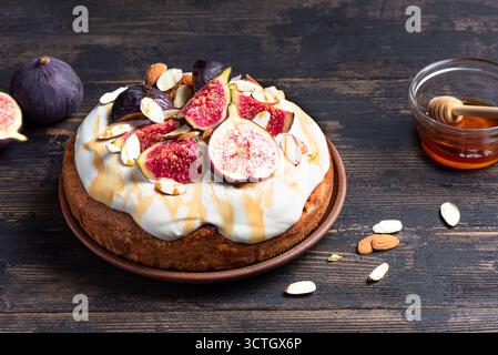 Pan di Spagna al miele con fichi, mandorle e formaggio cremoso montato su un tavolo di legno scuro. Ricetta per dolci di stagione per le vacanze autunnali. Foto Stock